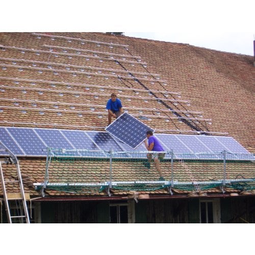 Zwei Arbeiter montieren Photovoltaik Anlage auf Dach, das mit grünem Netz abgesichert ist